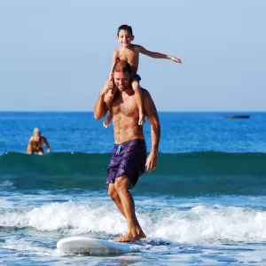 A man surfing with a child riding on his shoulders