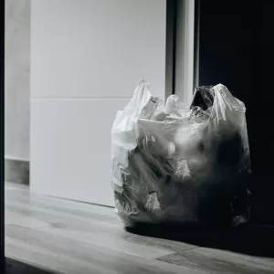 A dimly lit room containing a plastic bag filled with trash, emphasizing waste and recycling.
