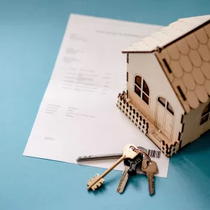 Miniature wooden house with keys and contract symbolizing real estate transactions.